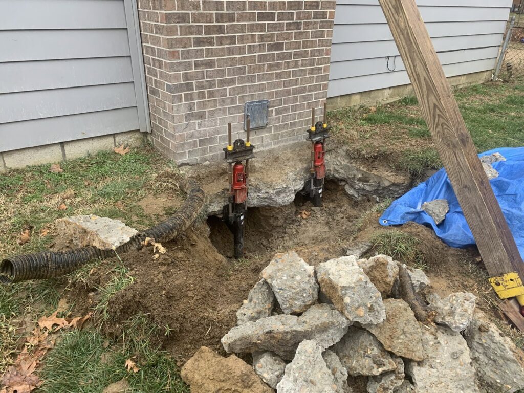 Two hydraulic jacks used for foundation lifting and stabilization next to a brick wall by Ram Jack Foundation Solutions in Hampton, VA.