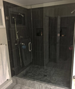 A frameless glass shower with dark tiled walls and a pebble floor, expertly installed by Lehigh Shower Glass in Bethlehem, PA