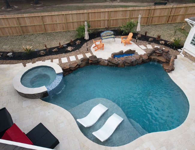 An aerial view of a freeform pool with an integrated spa and natural rock waterfall by Limitless Custom Pools and Backyards in Houston, TX.