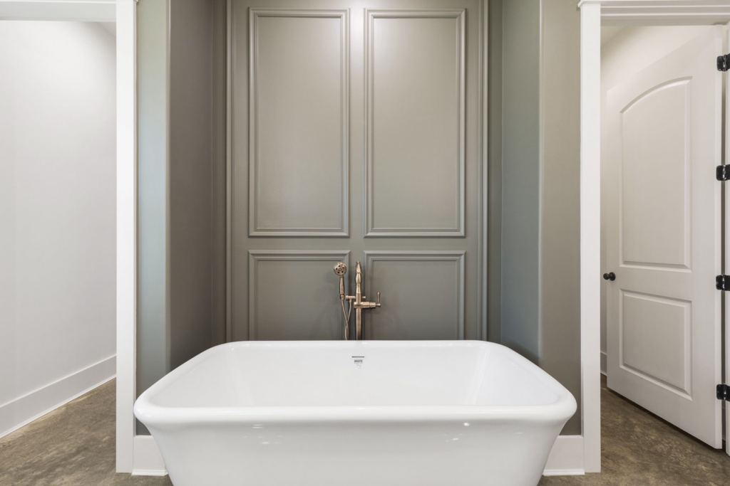 A freestanding white bathtub installation with grey paneled walls and a bronze faucet by Dugas Construction, LLC in Lafayette, LA.