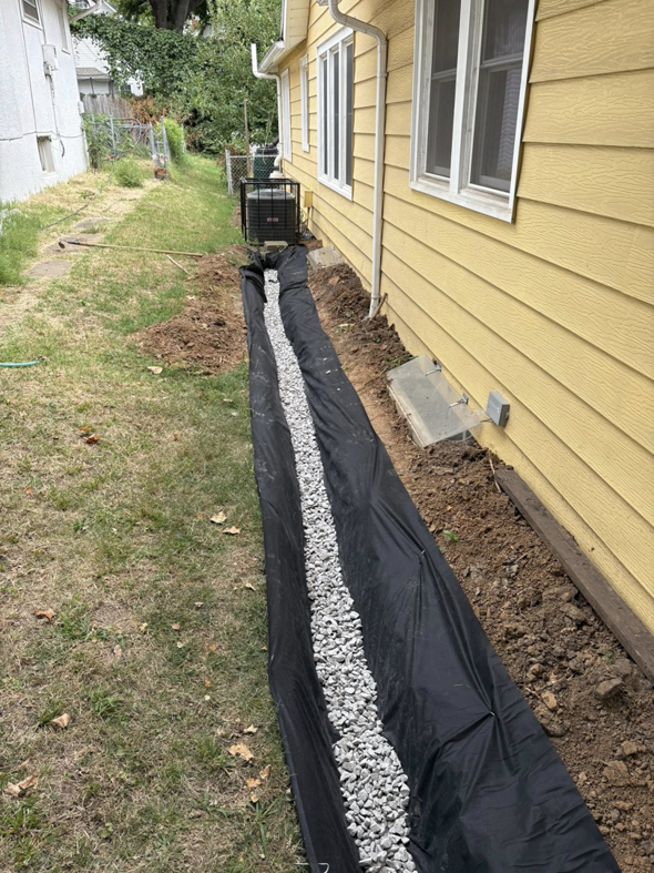 A newly installed French drain with gravel and landscape fabric alongside a house by Gama Home & Lawn Services LLC in Kansas City, MO.