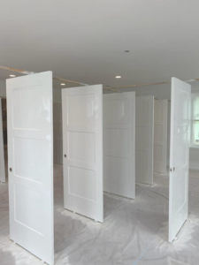 Several freshly painted white interior doors standing upright on a drop cloth by Desired Finishes in Ann Arbor, MI