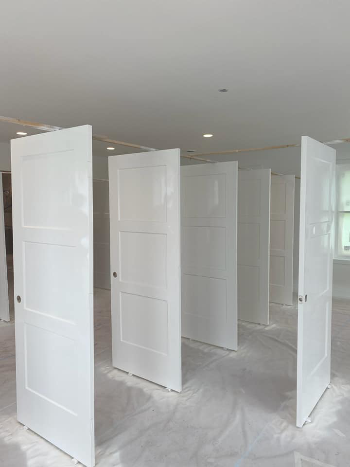 Several freshly painted white interior doors standing upright on a drop cloth by Desired Finishes in Ann Arbor, MI