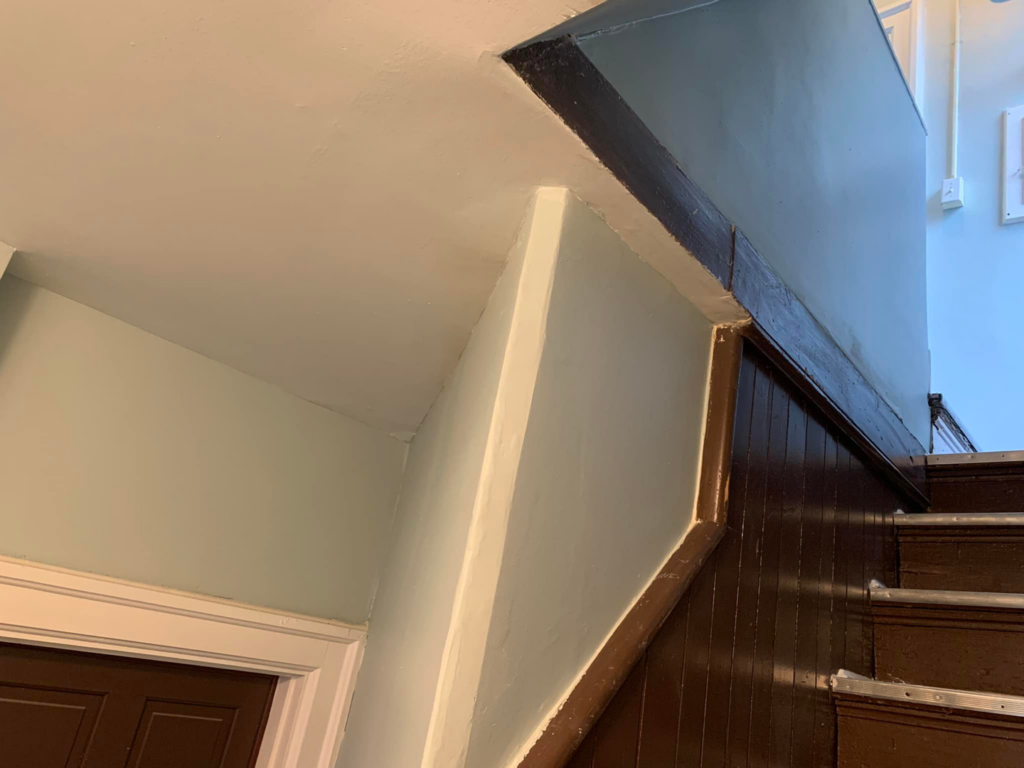 A freshly painted light blue wall alongside a dark wooden staircase, showcasing interior painting by PG Painting and Contracting Services in Cincinnati, OH.