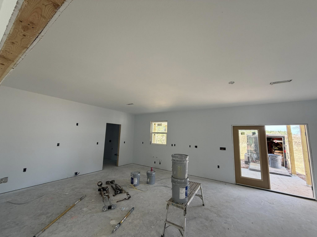 A room with freshly painted white walls and painting tools, demonstrating work by JM Drywall LLC in Dothan, AL.