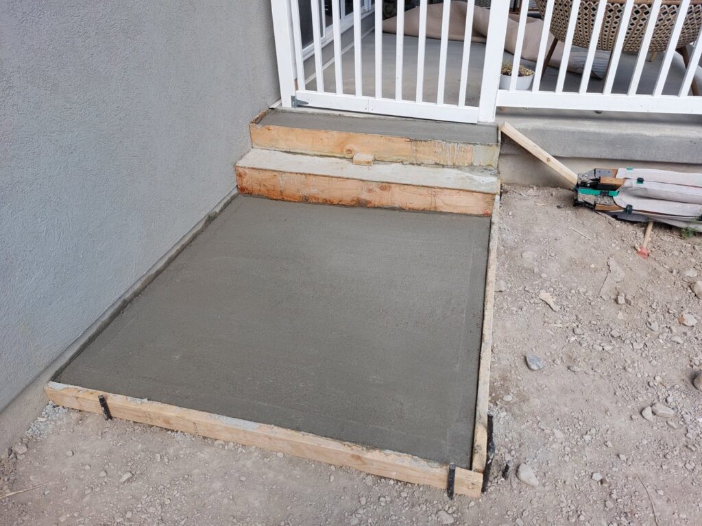 Freshly poured concrete steps and a small pad, framed with wood, demonstrating concrete work by Jake and Jake Construction LLC in Sandy, UT.