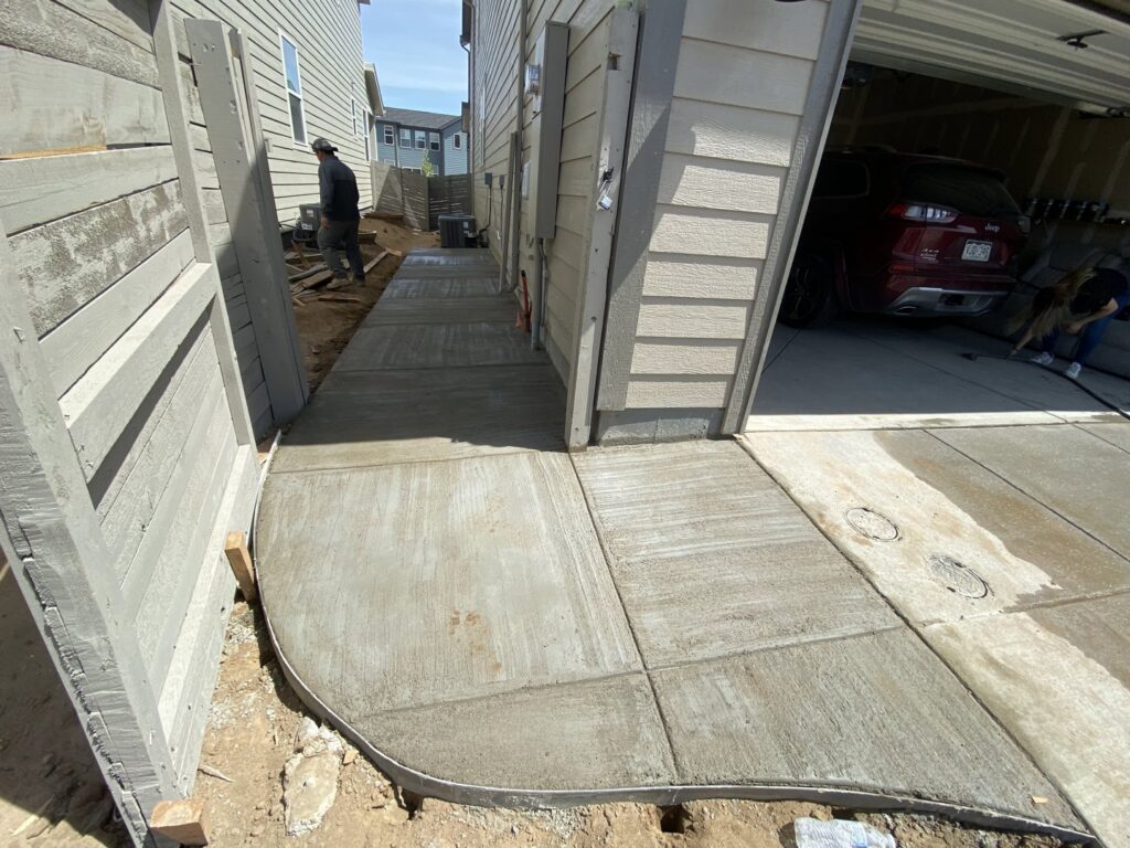 A freshly poured concrete walkway next to a residential garage, completed by Vazquez Quality Construction Inc in Aurora, CO.