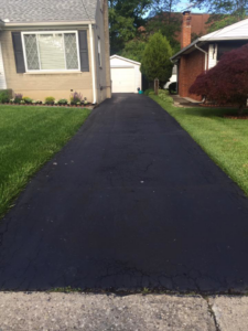 A freshly sealcoated asphalt driveway in front of a residential home by Cincy SealCoating in Morrow, OH.