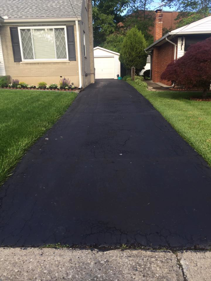 A freshly sealcoated asphalt driveway in front of a residential home by Cincy SealCoating in Morrow, OH.