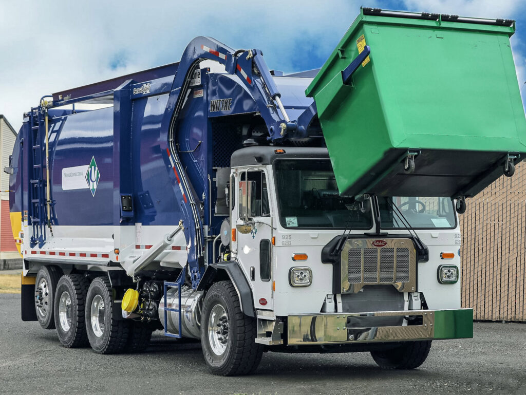 A Waste Connections front loader truck emptying a green commercial dumpster in Houston, TX, demonstrating general junk removal services.