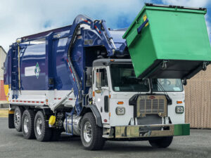 A Waste Connections front loader truck emptying a green commercial dumpster in Houston, TX, demonstrating general junk removal services.