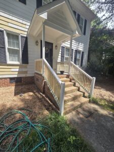 New wooden railings installed on a front porch with brick steps by Home FREA in Raleigh, NC.