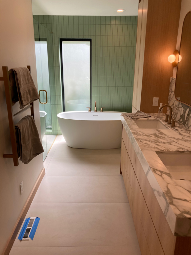 A beautifully renovated modern bathroom featuring a freestanding tub, green tiled wall, and double vanity by Tess Tile By Design in Kansas City, MO.