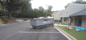 A Dump 'Em Dumpster Rentals dumpster full of debris in a parking lot next to a building in Charlotte, NC.