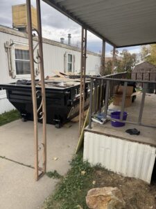 A DumpsterDash-LLC dumpster in Ogden, UT, filled with junk next to a mobile home, ready for pickup.