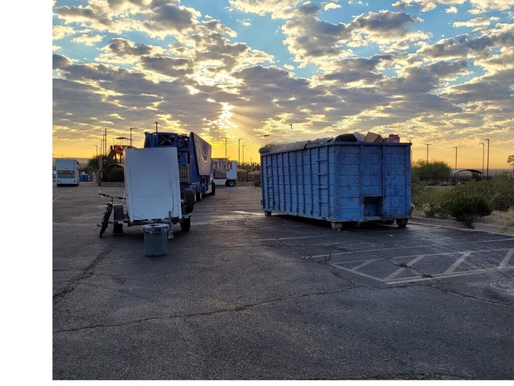 A blue Tidy up time dumpster, full of junk, parked in a lot at sunset, indicating a completed junk removal job in El Paso, TX.