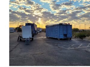 A blue Tidy up time dumpster, full of junk, parked in a lot at sunset, indicating a completed junk removal job in El Paso, TX.