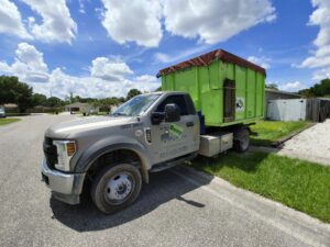 A truck picking up a full, covered green dumpster after a junk removal job by Bin There Dump That Dumpster Rental Orlando, FL.