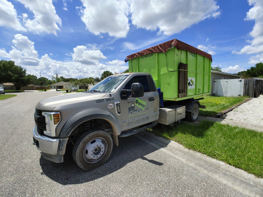 A truck picking up a full, covered green dumpster after a junk removal job by Bin There Dump That Dumpster Rental Orlando, FL.