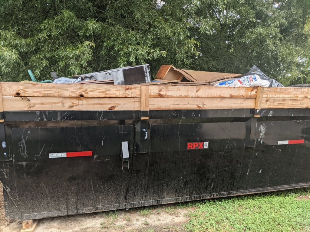 A black dumpster full of various residential junk and debris, provided by Standard Dumpster LLC in Rock Hill, SC.