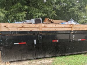 A black dumpster full of various residential junk and debris, provided by Standard Dumpster LLC in Rock Hill, SC.