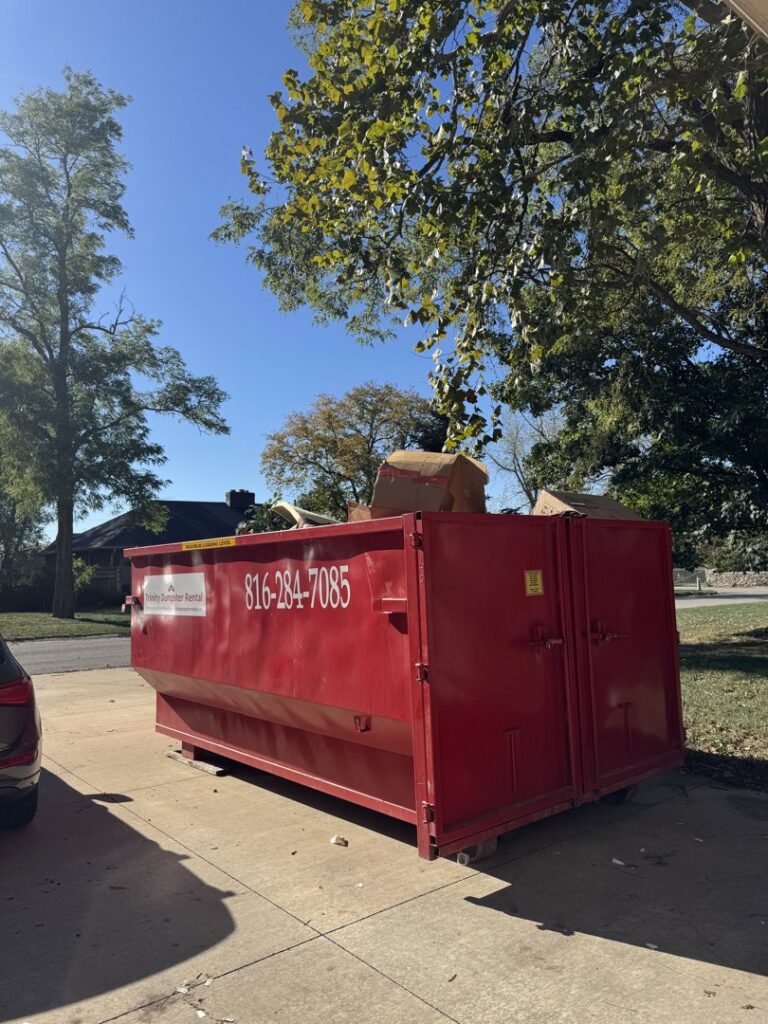A red dumpster full of debris from a residential junk removal project by Trinity Dumpster Rental LLC in Kansas City, MO.