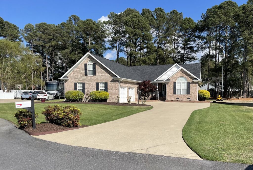 A full exterior view of a brick house with a long driveway, showcasing services by NC Siding and Windows in Raleigh, NC