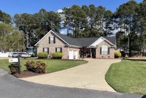 A full exterior view of a brick house with a long driveway, showcasing services by NC Siding and Windows in Raleigh, NC