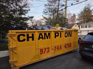 A yellow dumpster full of household junk and debris in a driveway, handled by Champion Waste Removal, Inc. in Orange, NJ.