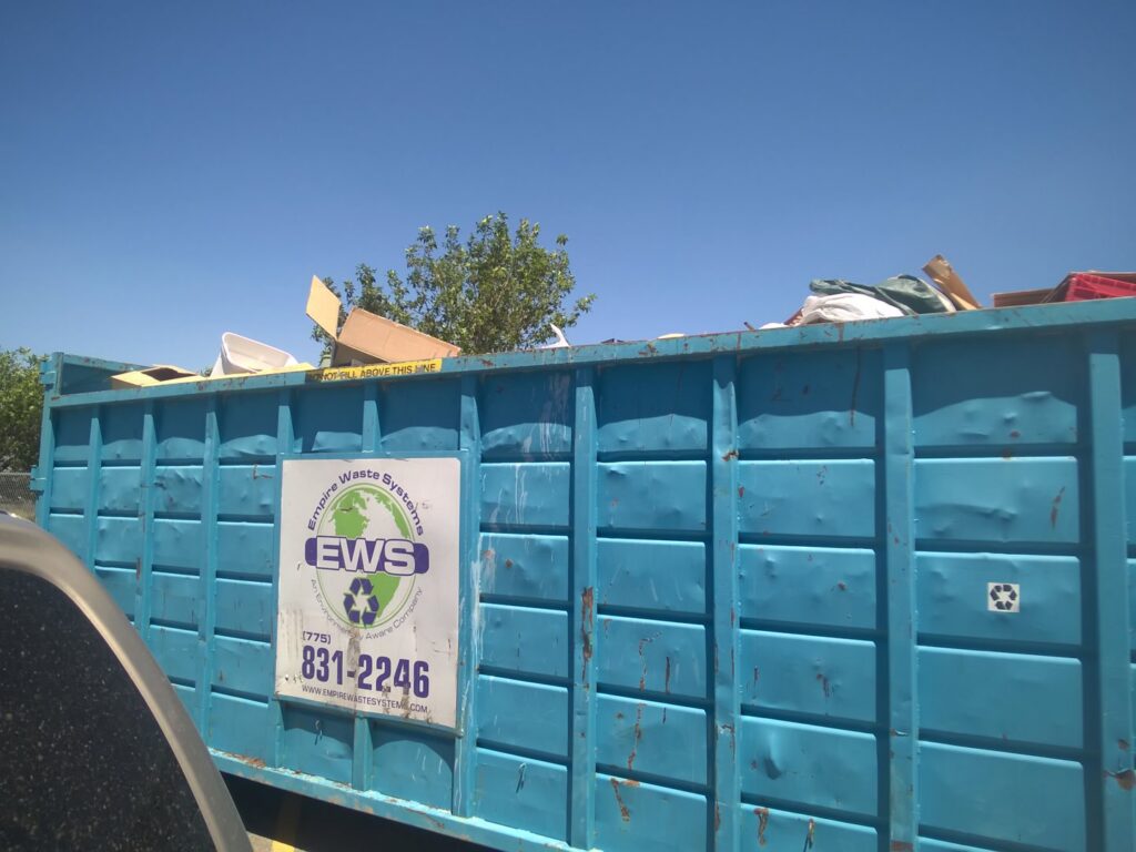 A blue roll-off dumpster from Empire Waste Systems in Carson City, NV, filled with various items for junk removal