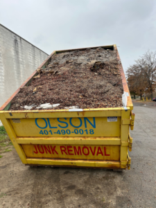 A large yellow dumpster filled with debris for junk removal by Greg Olson Trucking in East Providence, RI.