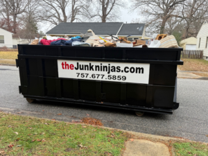 A large black dumpster overflowing with household junk on a residential street, provided by The Junk Ninjas in Hampton Roads, VA.