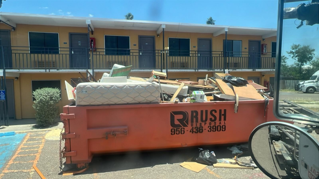 A Rush Disposal LLC dumpster overflowing with general junk and debris from a cleanup job in Laredo, TX.