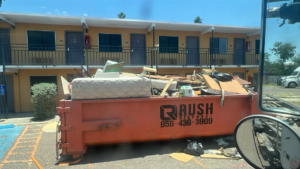 A Rush Disposal LLC dumpster overflowing with general junk and debris from a cleanup job in Laredo, TX.