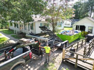 A full bright green dumpster on a trailer with a worker, ready for junk removal by Tristate Dumpsters LLC in Greenville, MS.