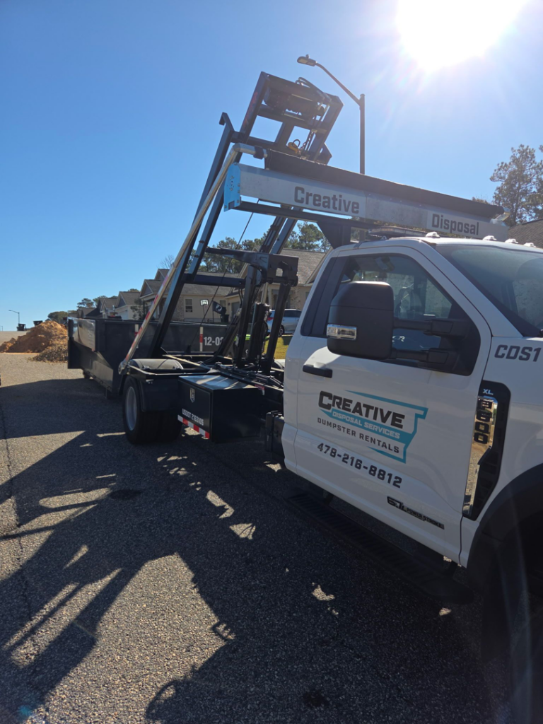 A Creative Disposal Services truck transporting a full dumpster of debris for junk removal in Macon, GA.