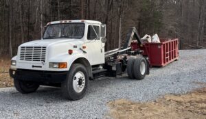 A Wallburg Disposal Worx LLC truck with a full red dumpster of junk on a gravel driveway in High Point, NC.