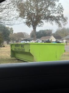 A bright green dumpster full of residential junk, ready for pickup by Tristate Dumpsters LLC in Greenville, MS.