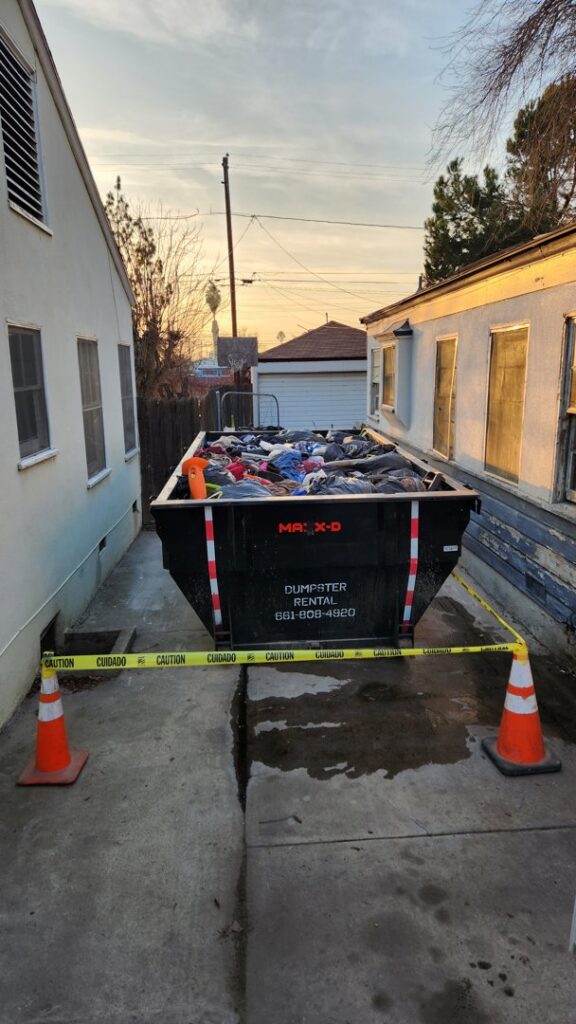 A full roll-off dumpster containing various junk and debris, secured with caution tape, for removal by Bakersfield Roll-Off Service in Bakersfield, CA.