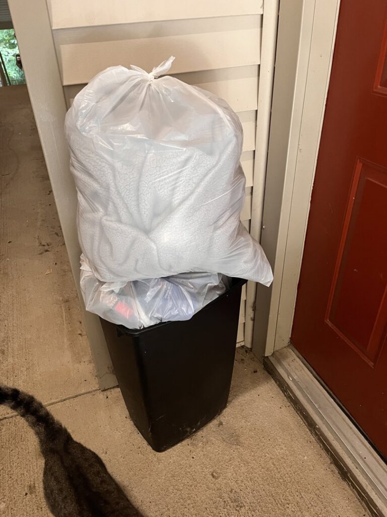 A full trash bin with a white bag on top, placed at a doorstep for A1 Valet Trash pickup in Atlanta, GA.