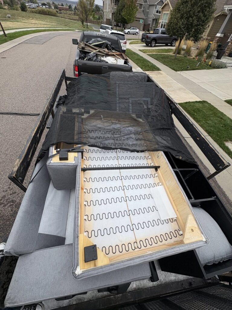 A trailer loaded with furniture frames and other items, covered with a net, ready for hauling by Goblins Junk Removal in Wheat Ridge, CO.