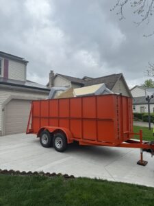 A Crazy Larry's Dumpster Rental trailer filled with old furniture and junk in a residential driveway in Columbus, OH.