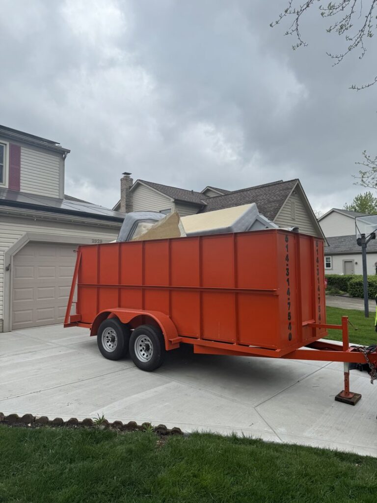 A Crazy Larry's Dumpster Rental trailer filled with old furniture and junk in a residential driveway in Columbus, OH.