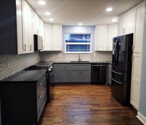 A remodeled galley kitchen with white and grey cabinets, chevron backsplash, and dark wood floors by Advanced Remodeling Services in Elbert, CO.