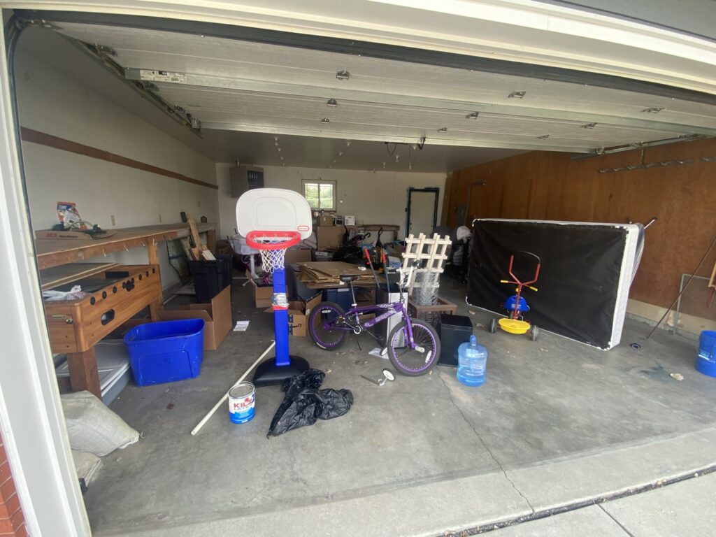 A garage filled with a basketball hoop, bicycle, and boxes, representing a 'before' scene for a garage cleanout by Empty It Out Junk Removal, LLC in Billings, MT.
