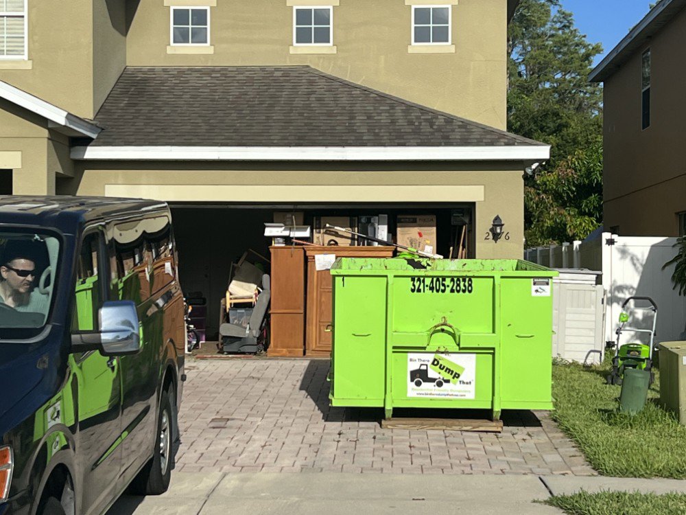 A green dumpster in a driveway, ready for a garage cleanout job by Bin There Dump That Dumpster Rental Orlando, FL.