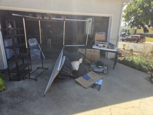 Various items including shelves, a lawnmower, and boxes piled outside a garage for cleanout by Titan Junk Co. in San Diego, CA