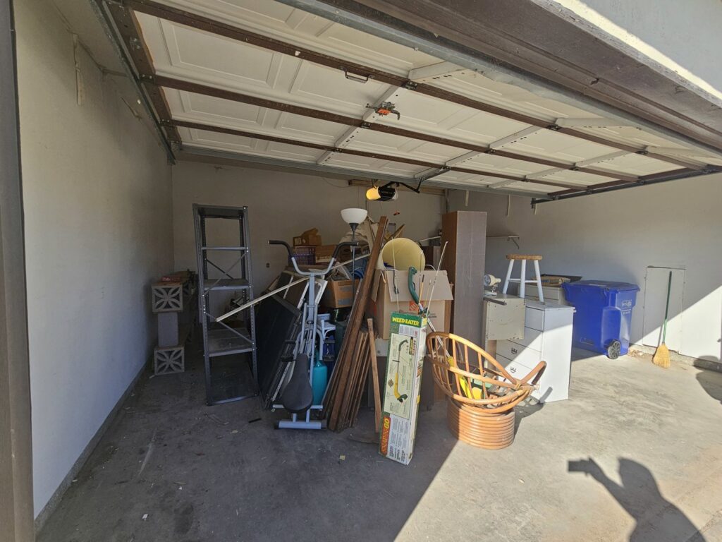 A cluttered garage filled with various items, boxes, and old furniture, indicating a junk removal job by Discount Hauling in Las Cruces, NM.