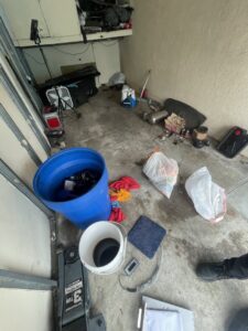 A garage undergoing a cleanout, showing junk, blue barrels, and other items for removal by Hazawaytoday.com in El Segundo, CA