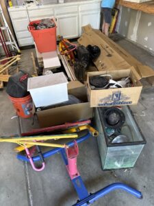 A cluttered garage floor with boxes, metal frames, and an aquarium, ready for junk removal by Goblins Junk Removal in Wheat Ridge, CO.
